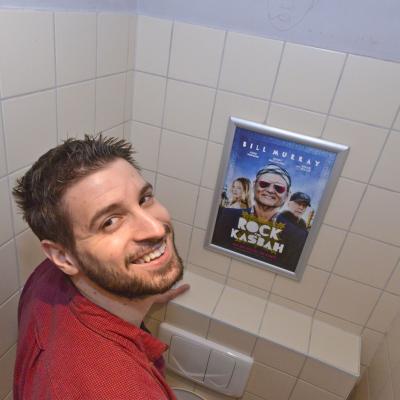 Filmwerbung als Poster mit Alurahmen auf heller Rückwand in Restaurant Toilette