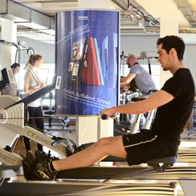 Beleuchtetes Poster hinter Mann am Rudergerät im Fitness Studio