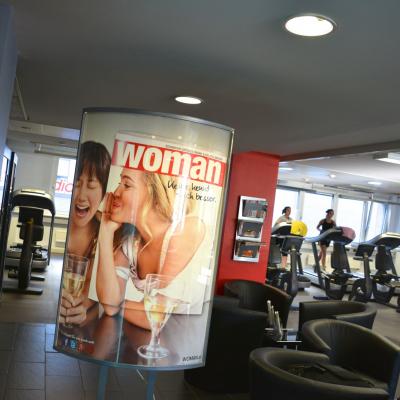 Beleuchtetes Werbeplakat für NEWS Abo im Fitness STudio, im Hintergrund Stepper und Räder