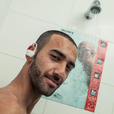 Mann steht im Fitness Studio unter Dusche mit Walkman, an den Kacheln Werbung für wasserdichten Sony Walkman