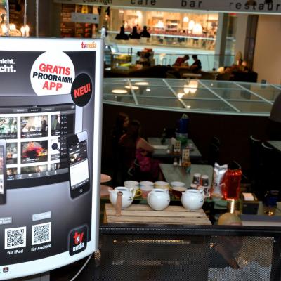 Beleuchtetes WerbePlakat für News Abo in Cafe Bar, neben Tresen mit Tee-Schalen