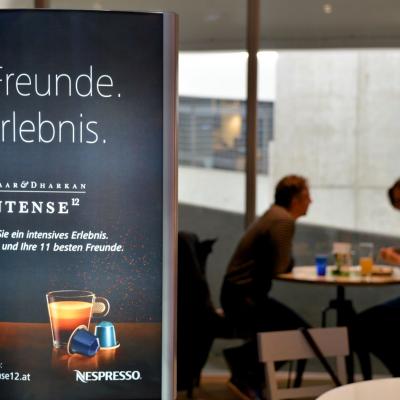 Weisse Schrift auf Schwarzem Werbeplakat, beleuchtet an der Wand, für Teekapseln von Nespresso in modernem Bar Restaurant mit großem Fenster im Hintergrund