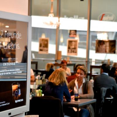 Weisse Schrift auf Schwarzem Werbeplakat, beleuchtet an der Wand, für Teekapseln von Nespresso in modernem Bar Restaurant mit großem Fenster im Hintergrund