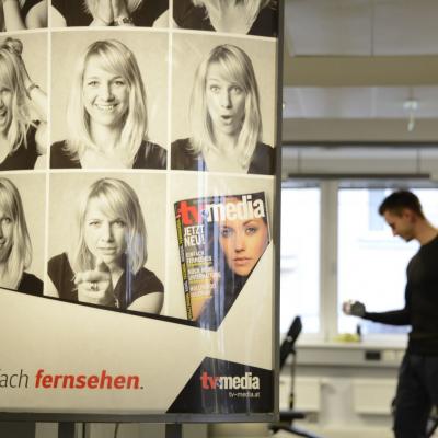 Werbung im Fitness STudio für NEWS Abos, im Hintergrund Mann beim Kardio-Training