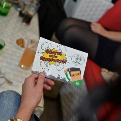 Postkarten mit Werbung für Bezirkszeitung in einer Hand gehalten in Bar Restaurant