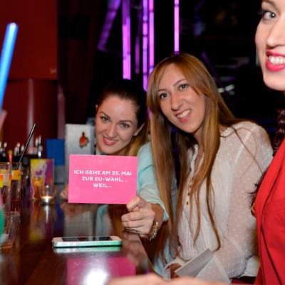 Junge Frauen halten eine rosa Postkarte mit Werbung für Neos in die Kamera
