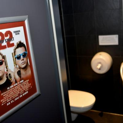 Filmwerbung in Alurahmen auf schwarzen Kacheln in Männertoilette Restaurant 