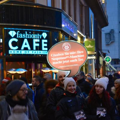 eine rote Sprechblase aus Kunststoff über dem Kopf eines Promotors in der Innenstatt, beleuchtet, bei Nacht