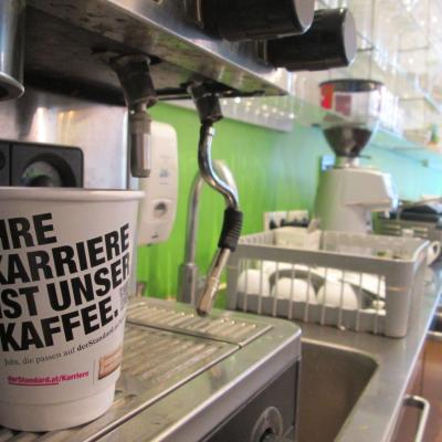 Kaffeebecher Kaffee zum Mitnehmen weiss mit Werbung in Bar auf Kaffeemaschine