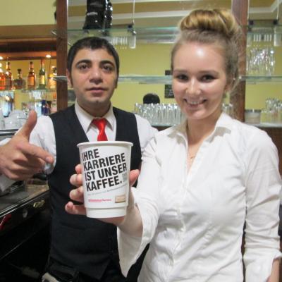 Kaffeebecher Kaffee zum Mitnehmen weiss mit Werbung in Bar in Händen von Verkäuferin