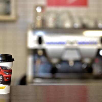 Kaffeebecher mit Werbung vor silberner Gastro-Kaffeemaschine