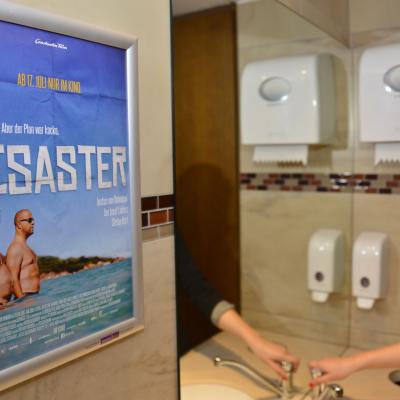 Poster mit Filmwerbung auf Restauranttoilette mit Alurahmen an dunkler Wand