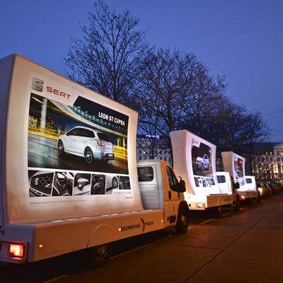 beleuchtetes 16 Bogen Plakat auf weissem Auto mit Werbung für Seat nachts im Großstadtverkehr