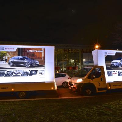 beleuchtetes 16 Bogen Plakat auf weissem Auto mit Werbung für Seat nachts im Großstadtverkehr