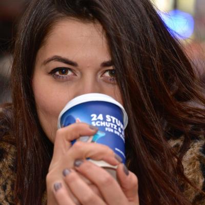 Frau trinkt aus Kaffeebecher unterwegs mit Nivea Werbung