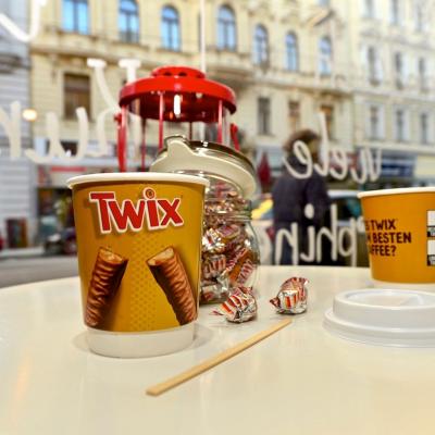 Kaffeebecher zum Mitnehmen mit Werbung für Twix in schicker Innenstadt Location