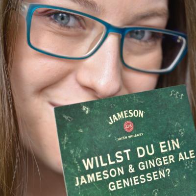 junge Frau hält grüne Werbepostkarte mit Werbung für Jameson in die Kamera
