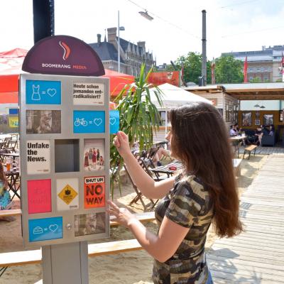 Junge Frau mit Werbepostkarte von Will Haben vor Postkartenständer in Gastronomie