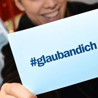 junger Mann hält hellblaue Werbepostkarte für die ERSTE BANK in die Kamera