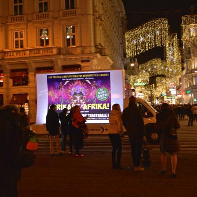 beleuchtetes 16 Bogen Plakat auf weissem Auto mit Werbung für Afrika! Afrika! nachts im Großstadtverkehr