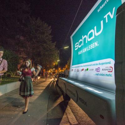 beleuchtetes 16 Bogen Plakat auf weissem Auto mit Werbung für schau TV nachts im Großstadtverkehr