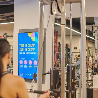 Digitaler Werbescreen im Fitnessstudio und trainierende Frau