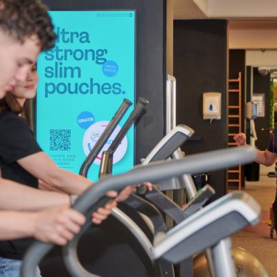 Menschen die in einem Fitnessstudio trainieren vor einem Werbescreen 